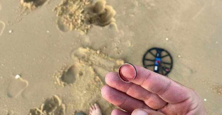 prospecteur qui vient de trouvé une bague sur un terrain difficile à la plage sur sable mouillé