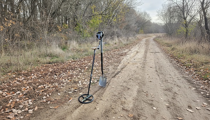 un détecteur DEUS posé contre une pelle au abord d'un chemin forestier