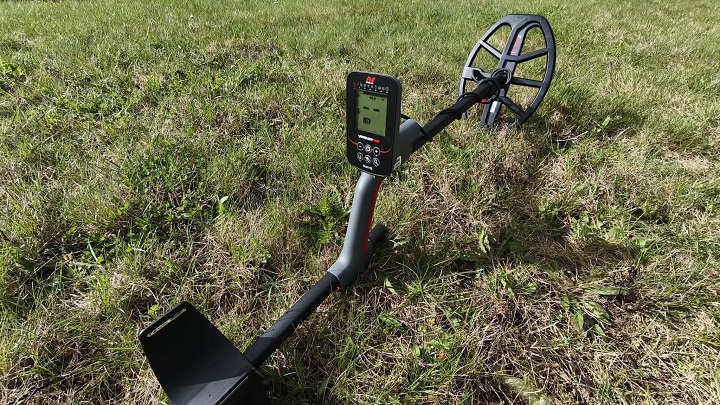 Minelab Vanquish 560 4 Détecteur de métaux Minelab Vanquish 560 complet avec sa canne télescopique et son disque V12X posé sur l'herbe lors d'un test sur le terrain.