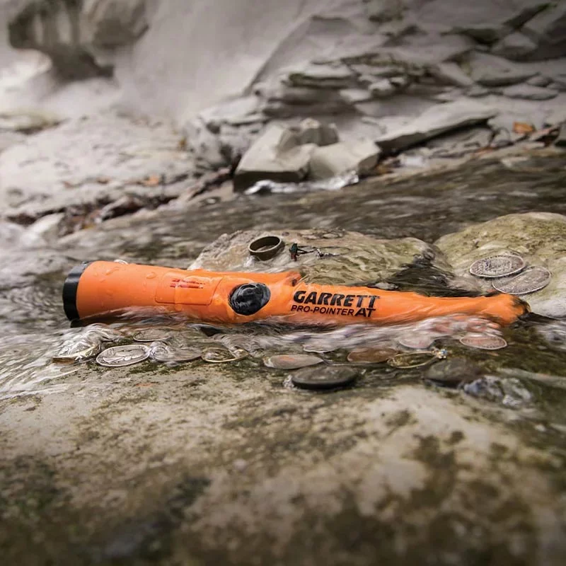 Garrett Pro-Pointer AT 2 Pointeur Garrett Pro-Pointer AT étanche orange posé dans l'eau d'un ruisseau au milieu de monnaies anciennes.
