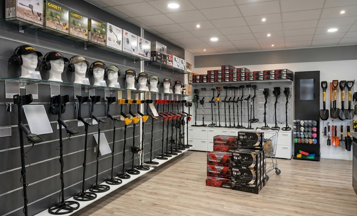 Détecteur et détection : acheter son détecteur moins cher ! 1 Intérieur d'un magasin spécialisé de détecteurs de métaux, montrant des modèles Garrett et Nokta Makro sur supports de sol, des casques audio sur têtes de mannequin, et des accessoires de détection comme des pelles, pinpointers.