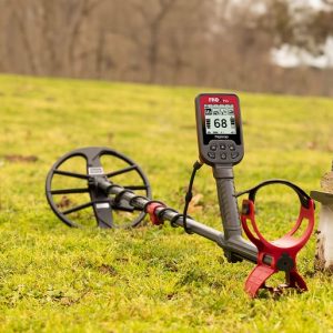 Détecteur de métaux Nokta FindX Pro en situation sur l'herbe, accompagné de son grand disque de détection et de son couteau de fouille.