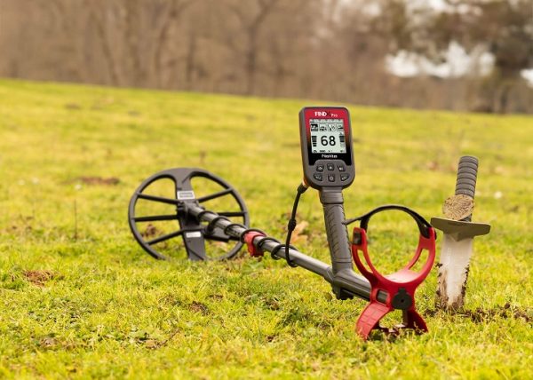 FindX pro : notre avis sur ce détecteur de métaux 6 Détecteur de métaux Nokta FindX Pro en situation sur l'herbe, accompagné de son grand disque de détection et de son couteau de fouille.
